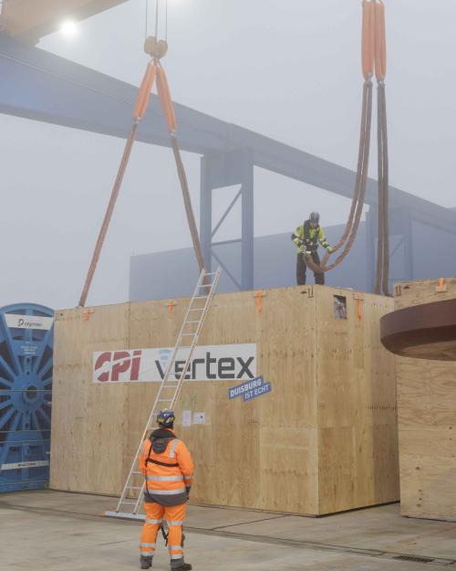 		Man standing on top of huge crate attaching a cable to it.
	