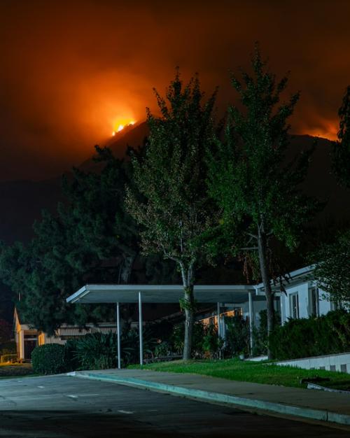 A house and garden in the foreground at night, with a wildfire glowing over a nearby hill