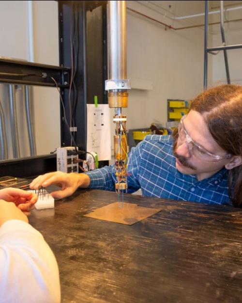 Three people wearing lab safety glasses look at a small scientific device