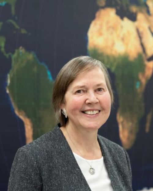 Ellen Lust, smiling, standing in front of a map of Africa