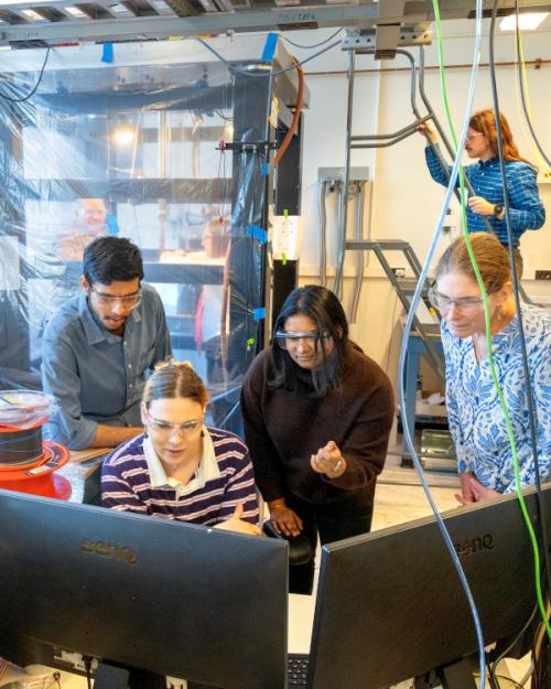 		Three people cluster around a computer in a science lab
	