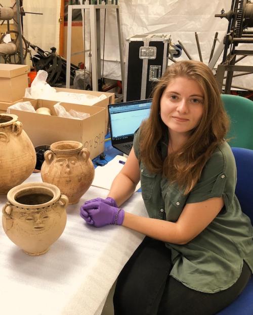 Person wearing laytex gloves sitting at a table with four ancient artifacts: pots