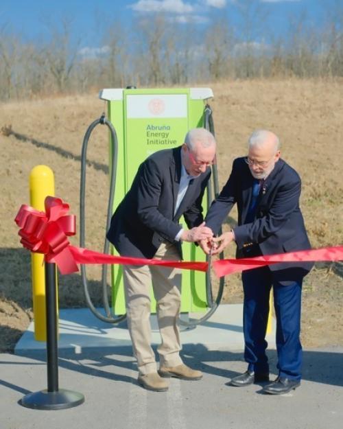 Two people cutting a red ribbon ceremonially. They are outdoors