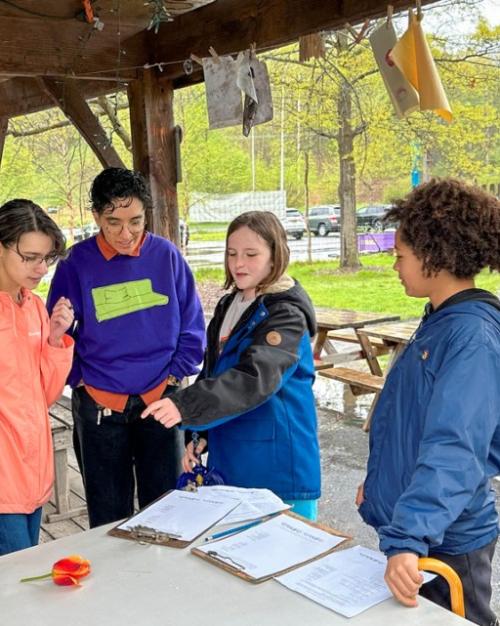 People cluster together in an outdoor shelter, looking at papers and flowers