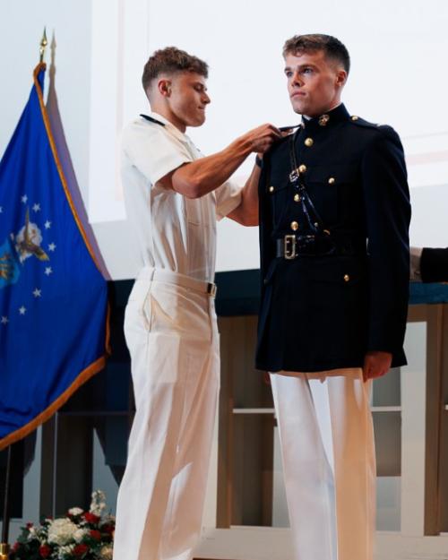 People on a stage; one in military uniform stands at attention