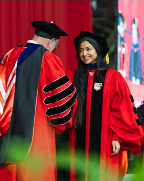 Person in academic robes shakes the hand of another person in academic robes
