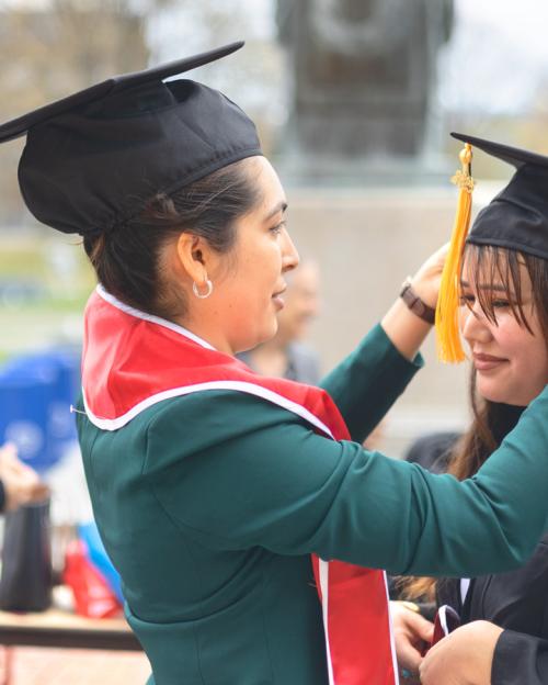 One person wearing graduation cap helps another with hers