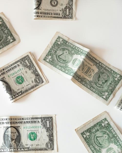 Dollar bills, some of them folded and crumpled, resting on a white surface