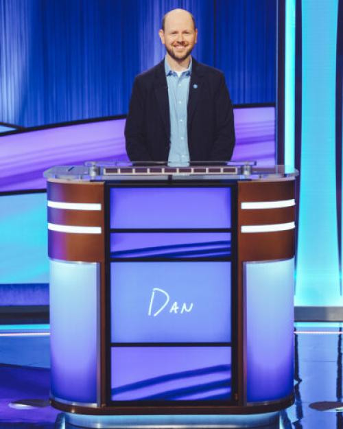 Dan Moren, mostly bald with a beard and a smile, standing at the Jeopardy podium with the word "Dan" on it