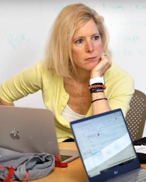 person at a desk with computers, looking thoughtful