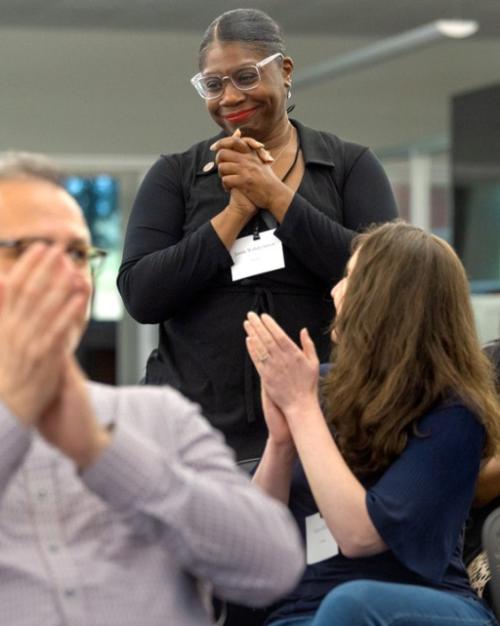 People in an audience applaud one person standing