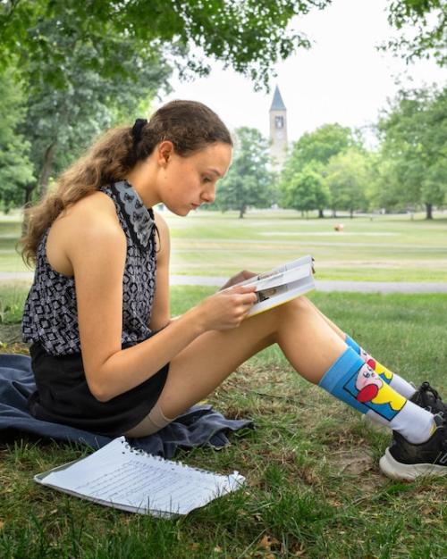 		Person sitting on grass, reading a book propped on knees
	