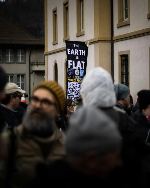 A sign sticks out from a crowd of people, saying "the Earth is flat)