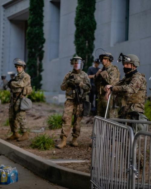 people in military fatigues stand by the side of a street