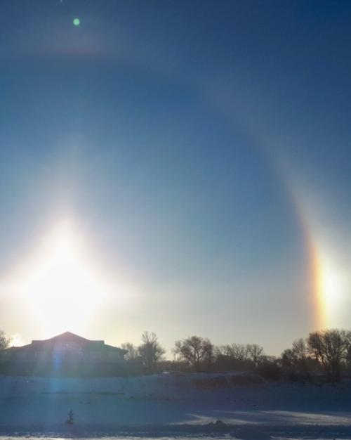 In the sky, a perfect half circle appears around a rising sun with two bright "sun dogs" on either side
