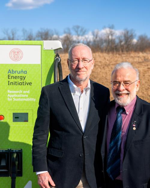 Two men sitting in front of an electrical vehicle charger on campus