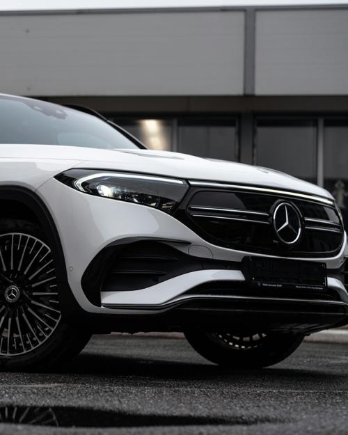 A white electrical Mercedes Benz car against a gray building