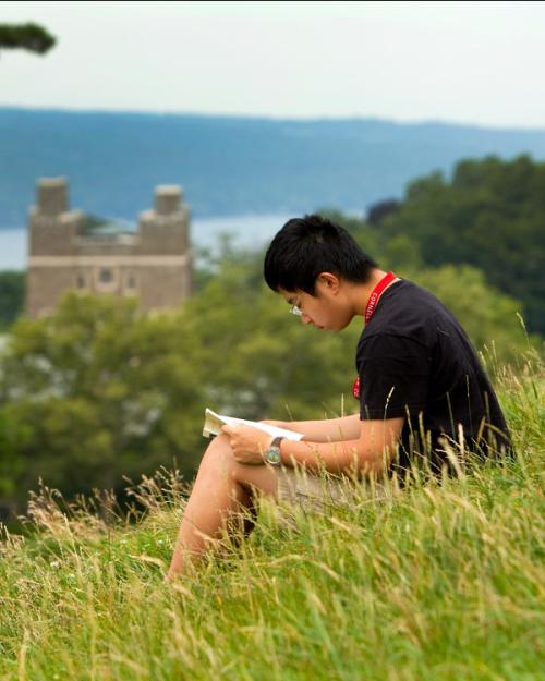 Person sitting in tall grass on a hilside, reading a book