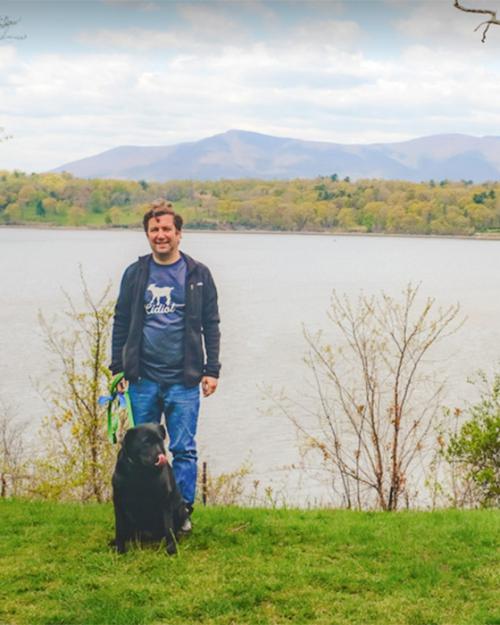		Person standing with a dog on the bank of a river
	