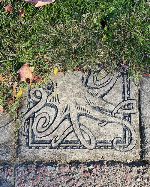 		Close up of a paving stone carved with an octopus, next to grass
	
