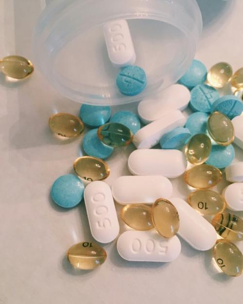 close-up of pillls of sevreal sizes and colors, spilling out of a bottle