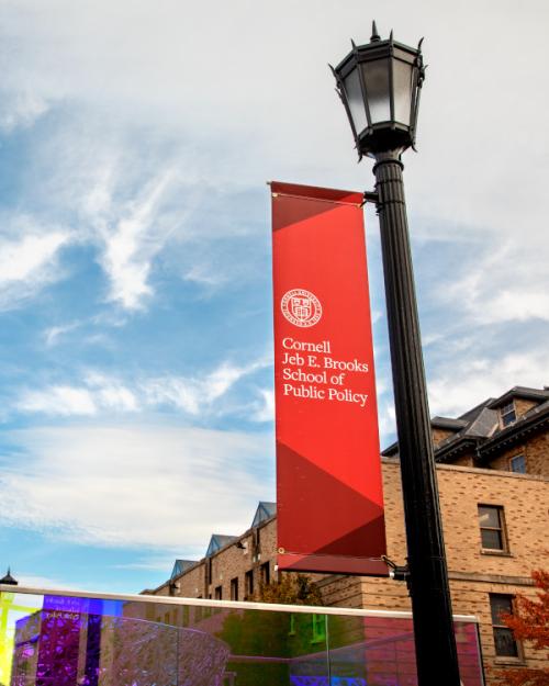 Lamp post with a red banner attached: Cornell Jeb E. Brooks School of Public Policy