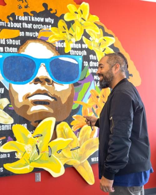 Two people stand with a colorful mural between them