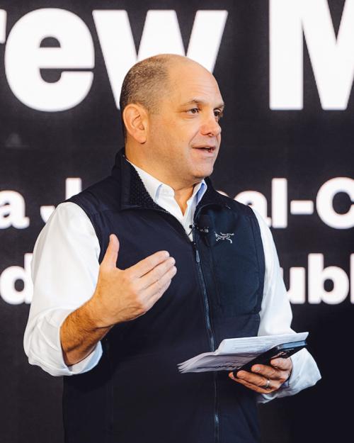 		Person wearing a black vest and white shirt, speaking publically
	