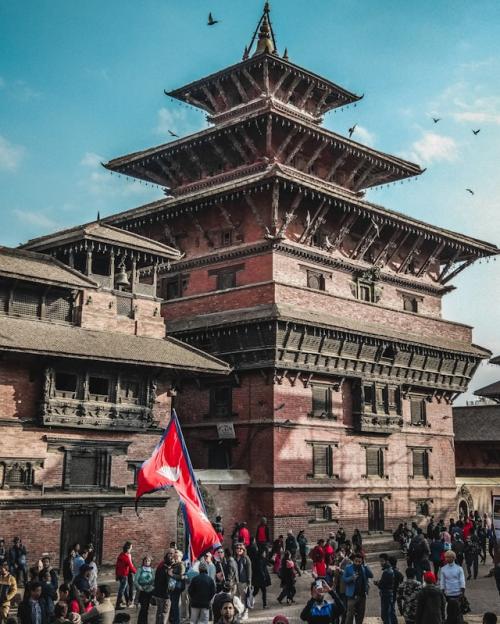 		People standing in front of a big brick building with three levels of pagoda-style roofs
	