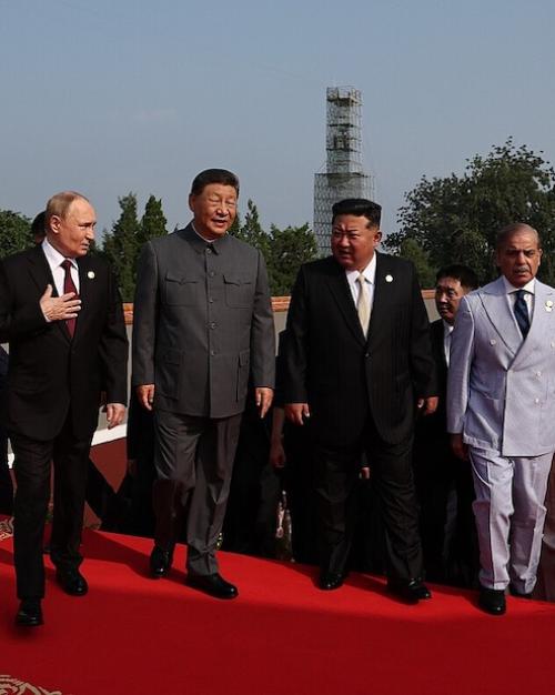 Six people in suits walk abreast up a red carpet, conversing