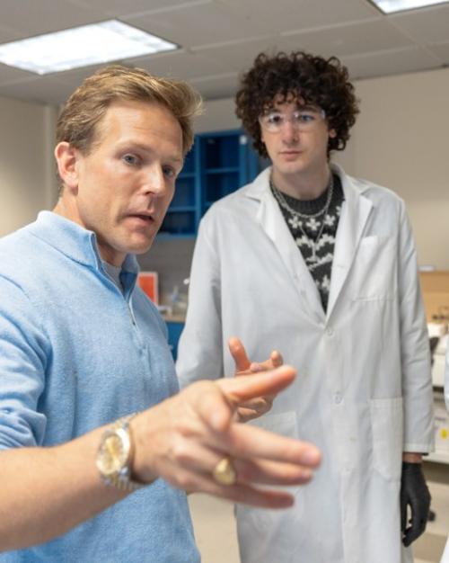 		three people; two in lab coats, looking at the third, who is pointing instructively
	