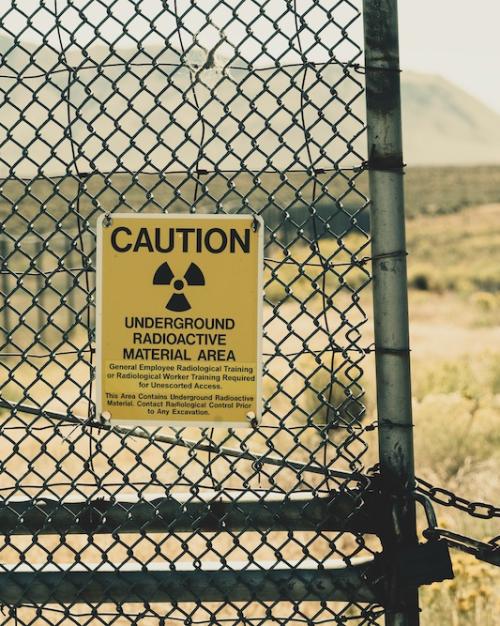 Chain link fence with yellow warning signs: CAUTION, UNDERGROUND RADIOACTIVE MATERIAL AREA