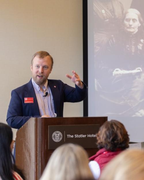 Person speaking at a lecturn with a black and white photograph displayed behind