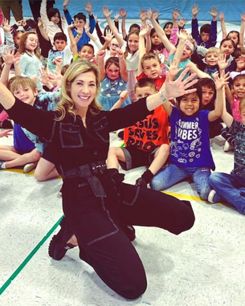 Person in black jump suit poses in front of a crowd of excited children