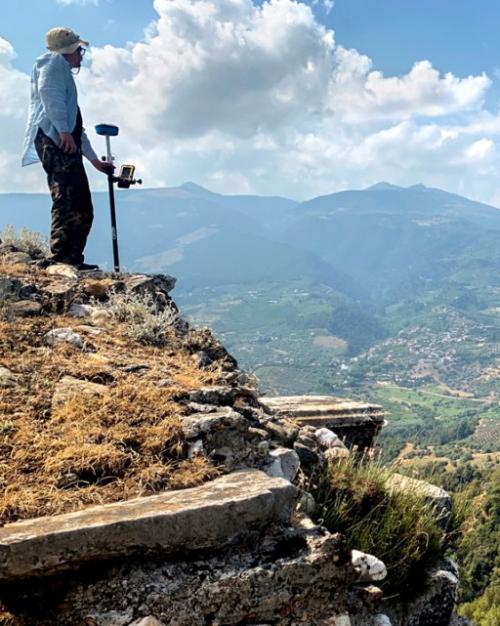 Person standing on a rocky hill, looking out over a huge, green plain