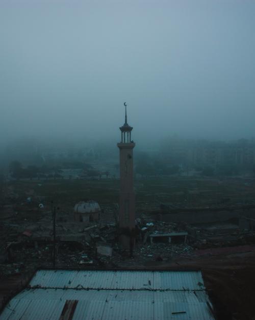 mosque spire rises in fog over a war-damaged street