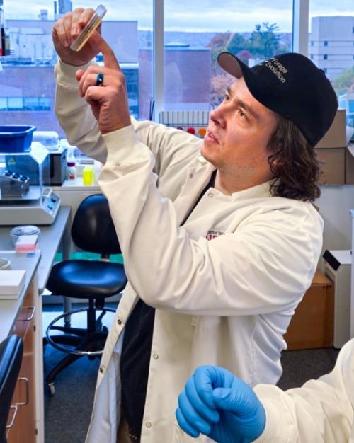 Two people work in a lab, looking up a a tube