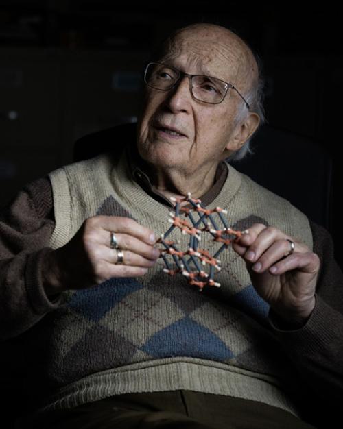 Artistic portrait of a person in argyle pattern sweater vest holds a small model of a molecule and looks pensive