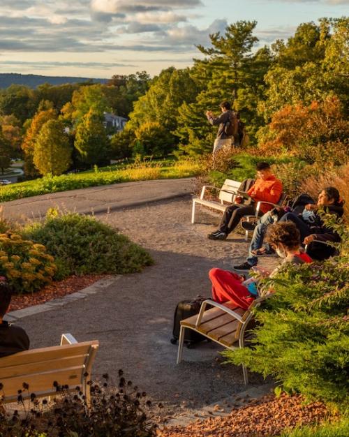 People sitting on benches, reading with a lake and forest vista in front of them