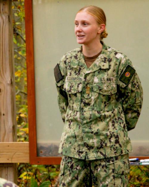Person in military fatigues standing in front of others, speaking