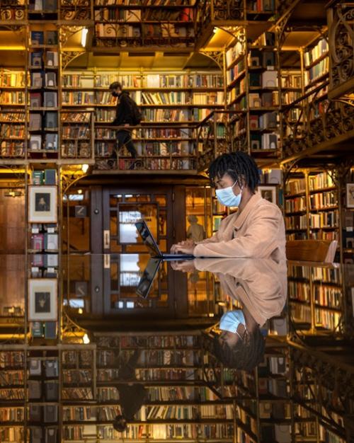 		Two people sitting at a table, reading in a room full of books on shelves; the books are reflected on the surface of the table, creating a sense of immersion
	