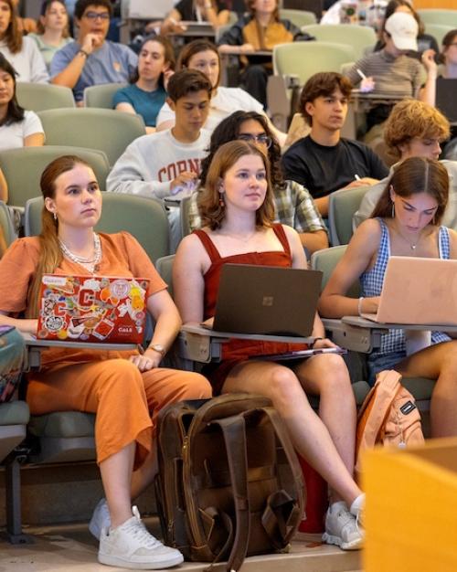 Dozens of college students sit at attention in an auditorium with tiered seating