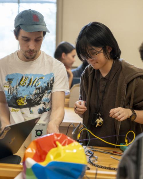 		About five students cluster around a table full of equipment in an introductory physics lab
	