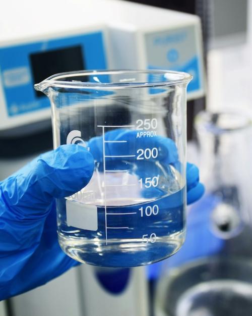 hand in a blue glove holding a beaker with clear liquid in it