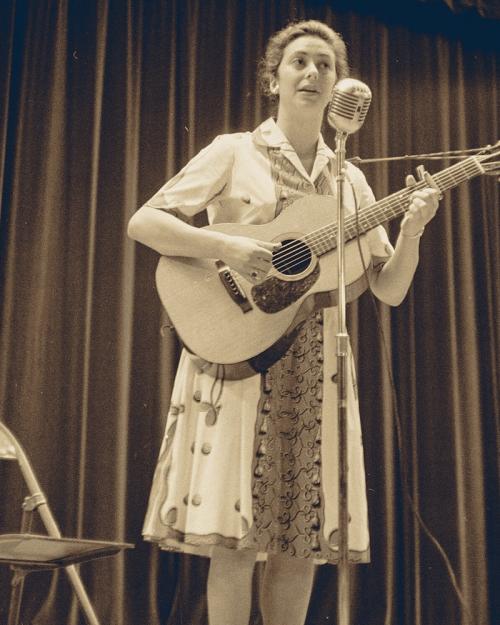 Black and white historic photo of a person playing a guitar and singing into a microphone