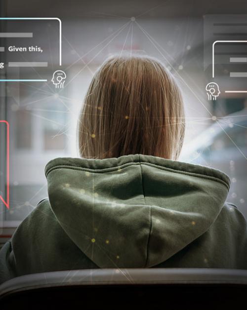 Seen from the back a person wearing large hooded sweatshirt faces a computer screen