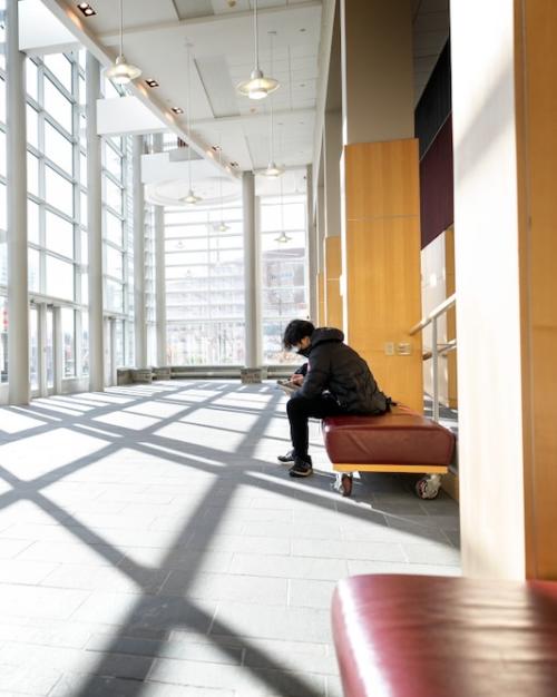 person reading on a bench in a large, sunny, modern room