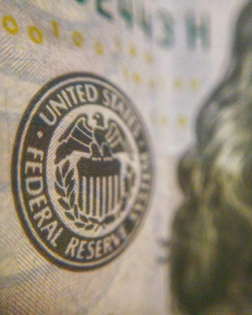 Circle on textured paper that says 'Federal Reserve'; an extreme close up of a one-dollar bill, US