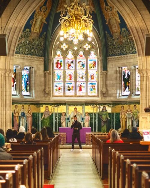 Colorful interior of a chapel with a vaulted ceiling; people sit in the pews facing a person speaking at the front
