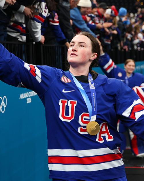 Person in a blue USA jersey reaches up to slap hands with a member of the crowd, celebrating